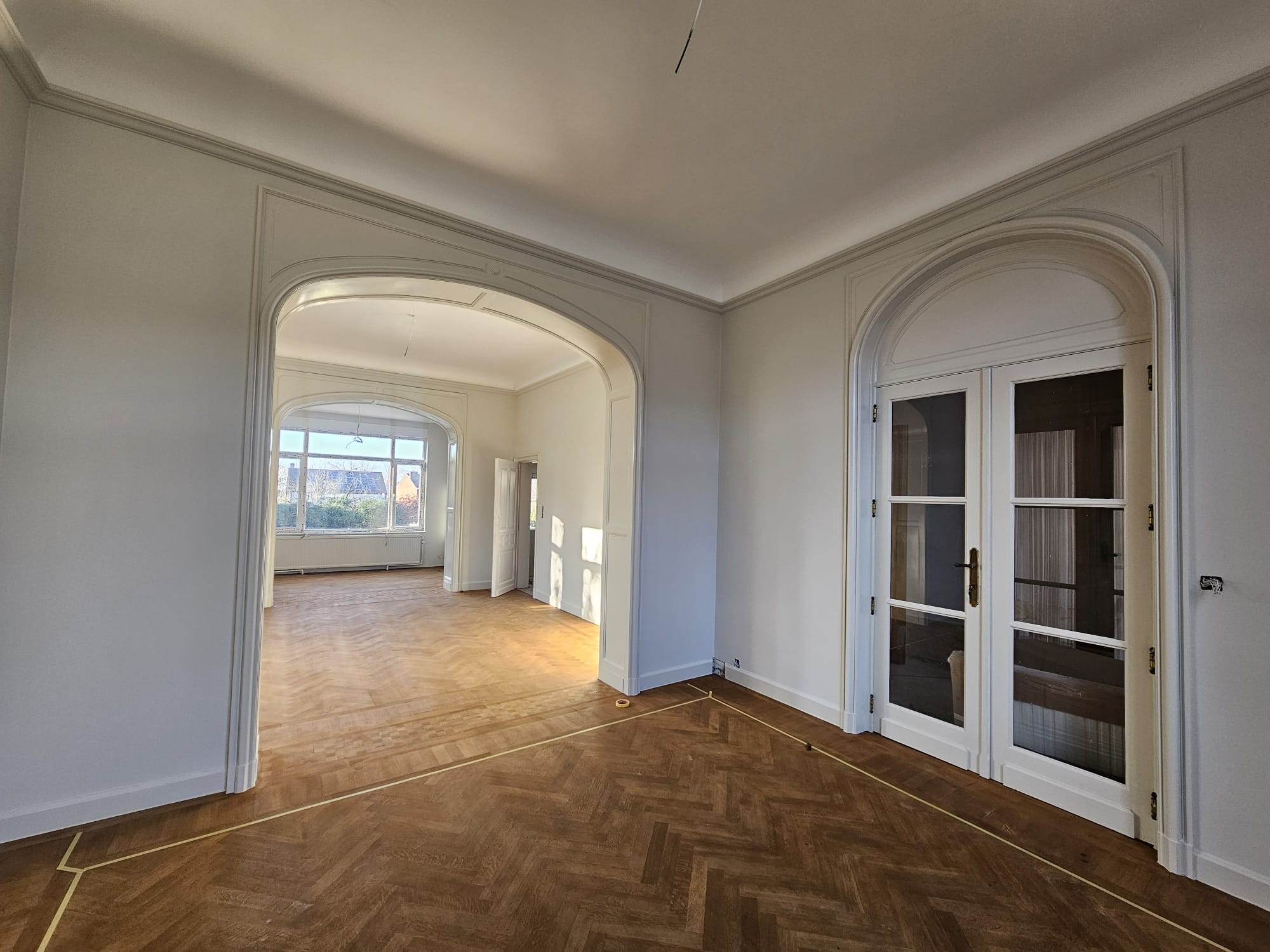 Pièce à moulures et arches repeintes en blanc, parquet à chevrons