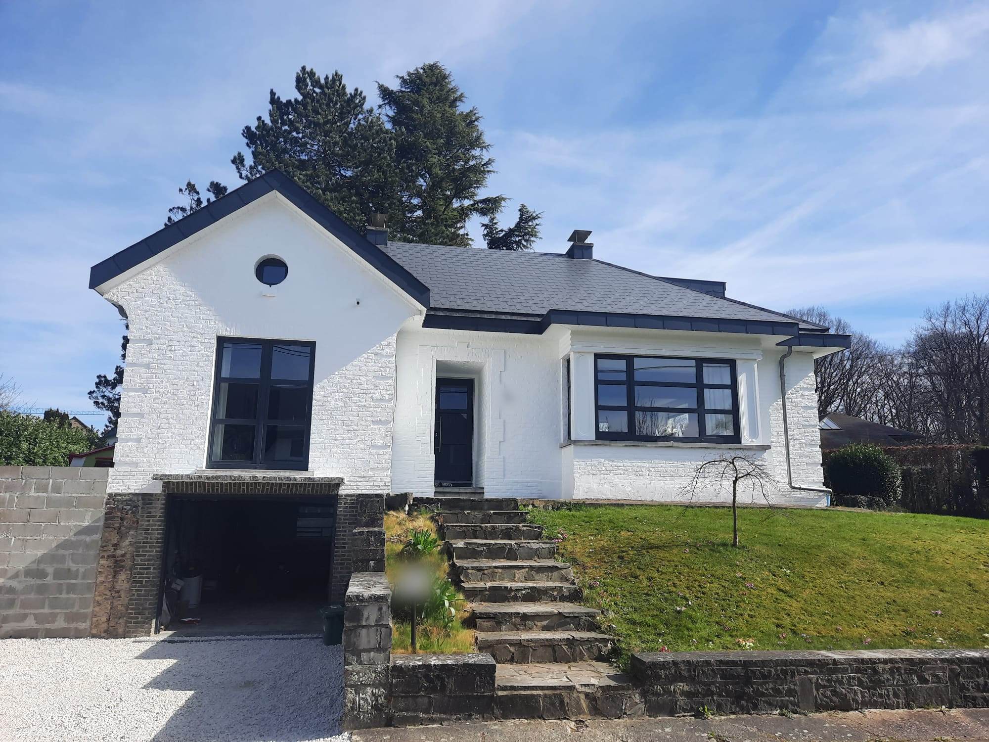 Maison à façade blanche et châssis noirs après travaux